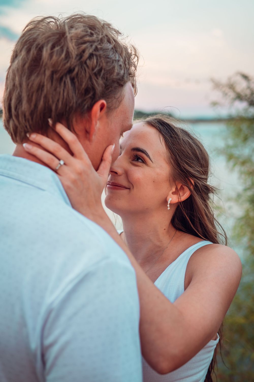 Romantic couple in light colored clothing share an intimate moment against a sunset backdrop.