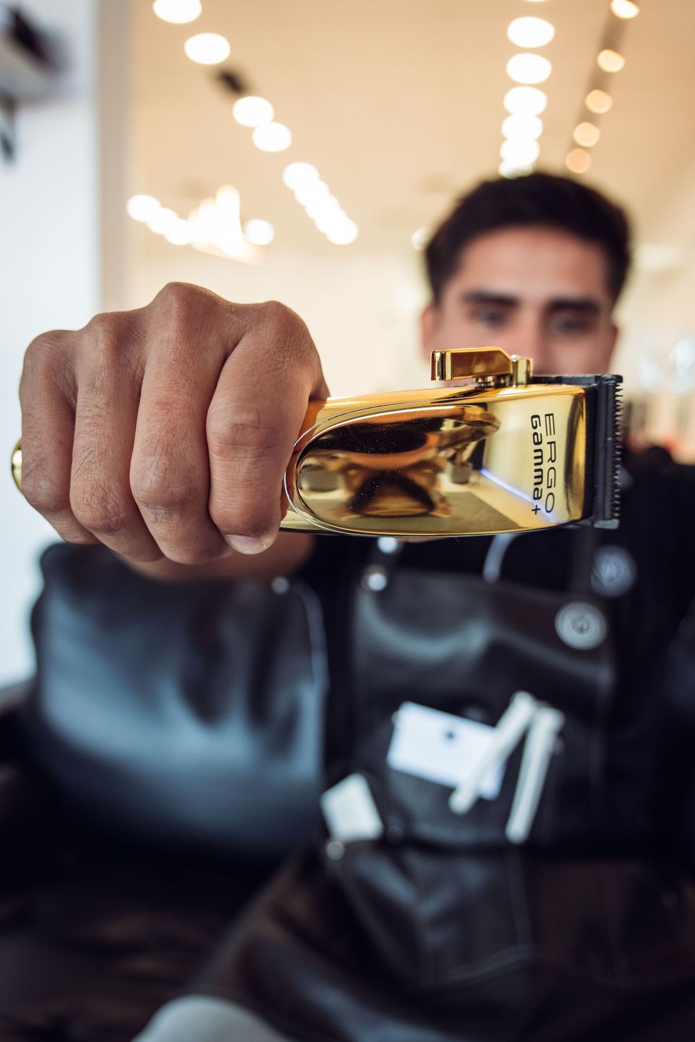 Gold-plated hair clipper held up in focus with blurred salon interior.
