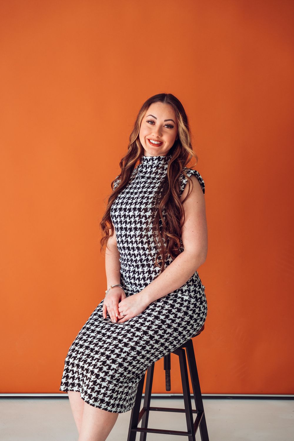 Stylish houndstooth dress outfit shown against vibrant orange wall backdrop.