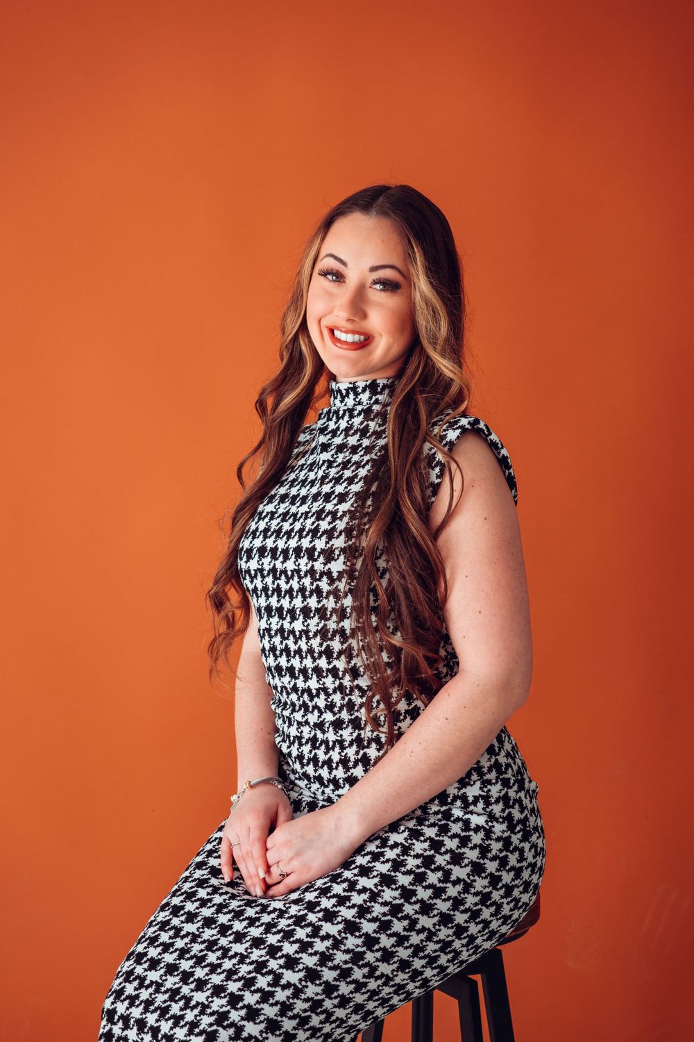 Elegant houndstooth pattern dress styled with long wavy hair against orange background.