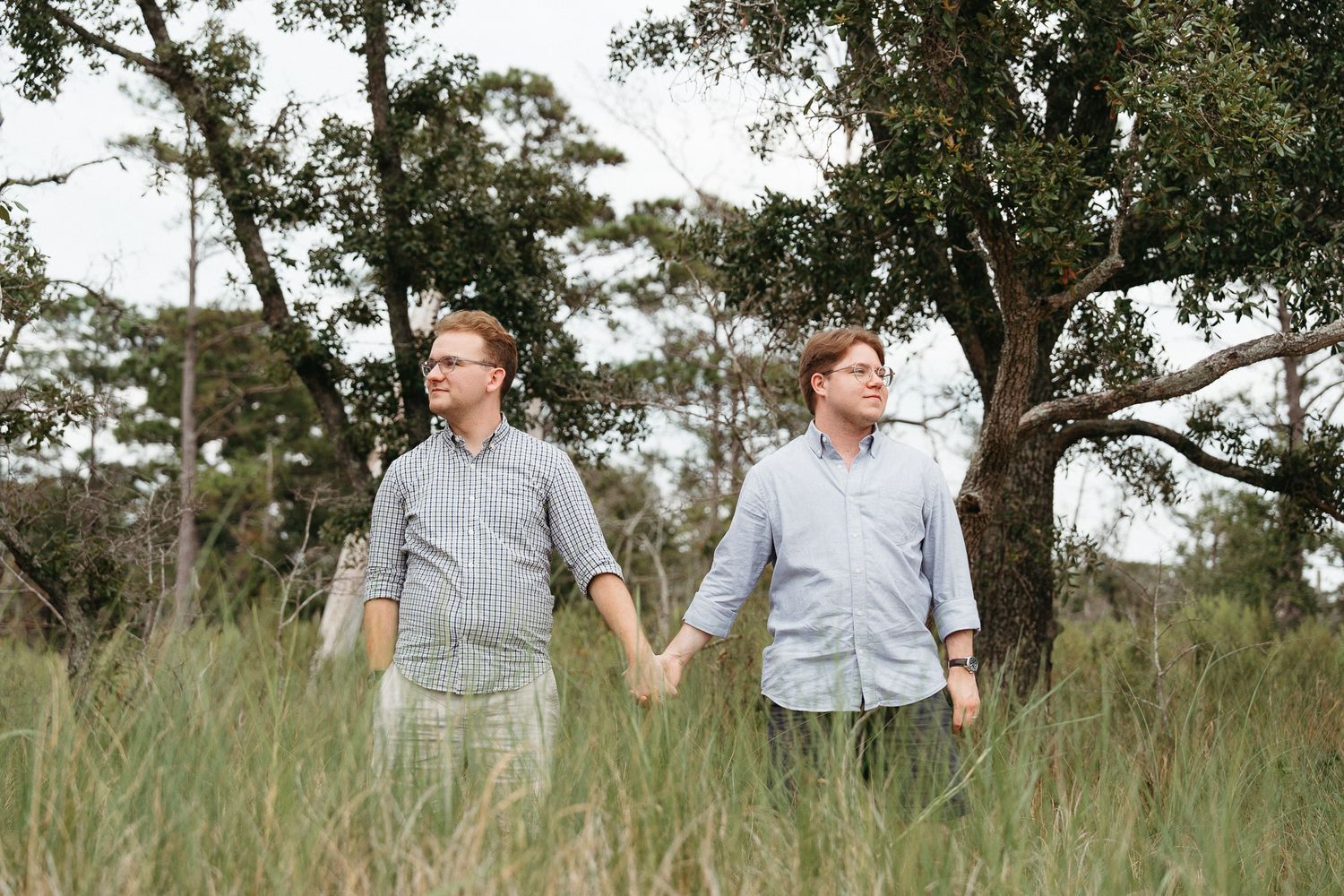 A couple walks hand in hand through a sunlit meadow in Carolina Beach, NC. Gay Couples photographer. Surprise Proposal