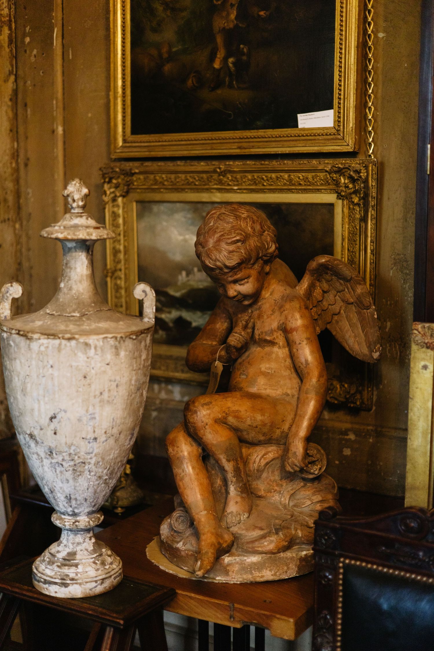 Antique cherub statue and decorative urn displayed in elegant interior setting.