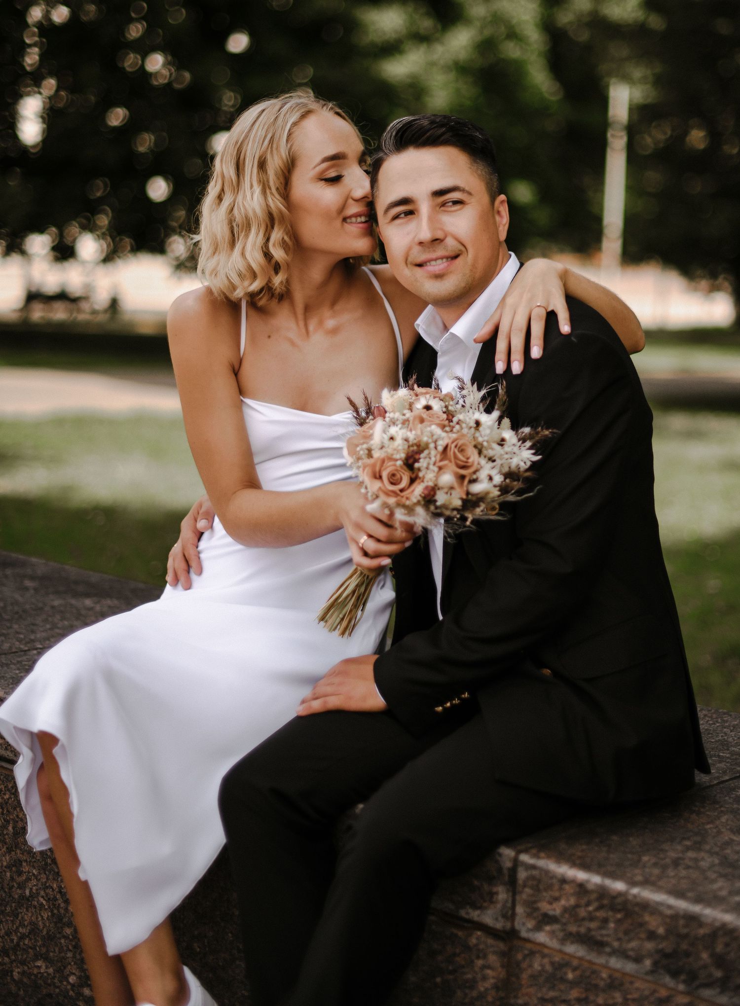 Wedding couple sharing an intimate moment outdoors with a pastel bouquet.