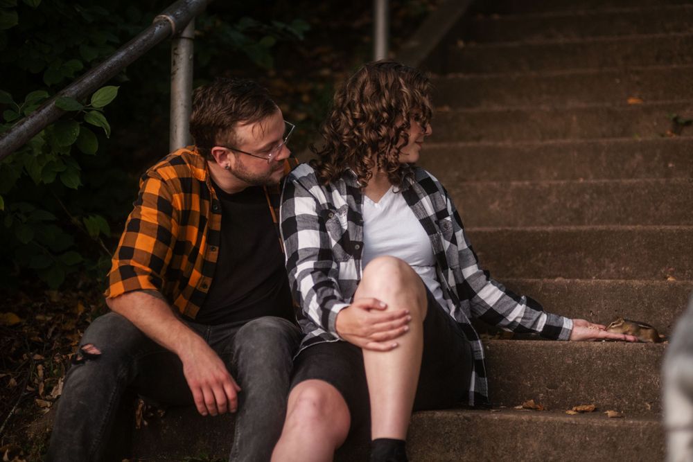 Two people wearing plaid flannel shirts sit together on outdoor stone steps in a romantic moment.