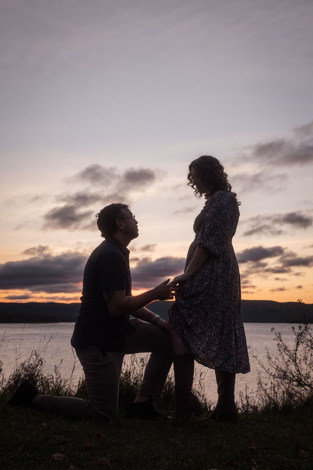 A silhouetted couple shares a romantic proposal moment at sunset by a tranquil lake.