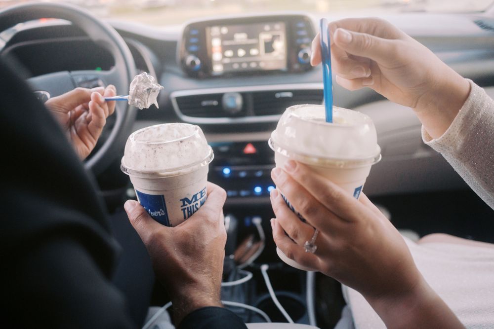 Two people in a car holding iced beverages in disposable cups with straws.