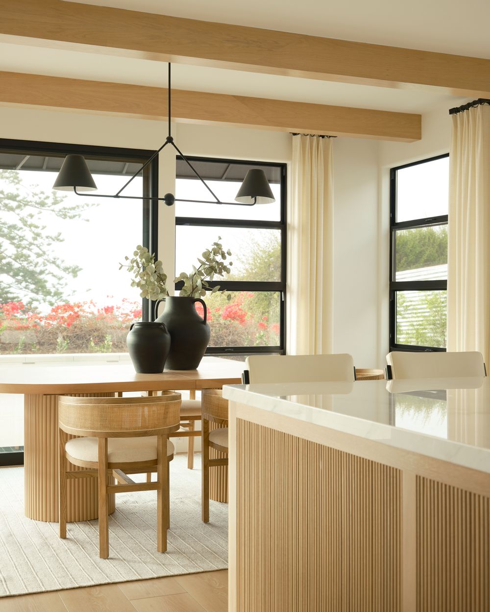 Contemporary open dining area with wood ceiling beams, black-framed windows, and pendant lighting — photographed by Khoi Ly.