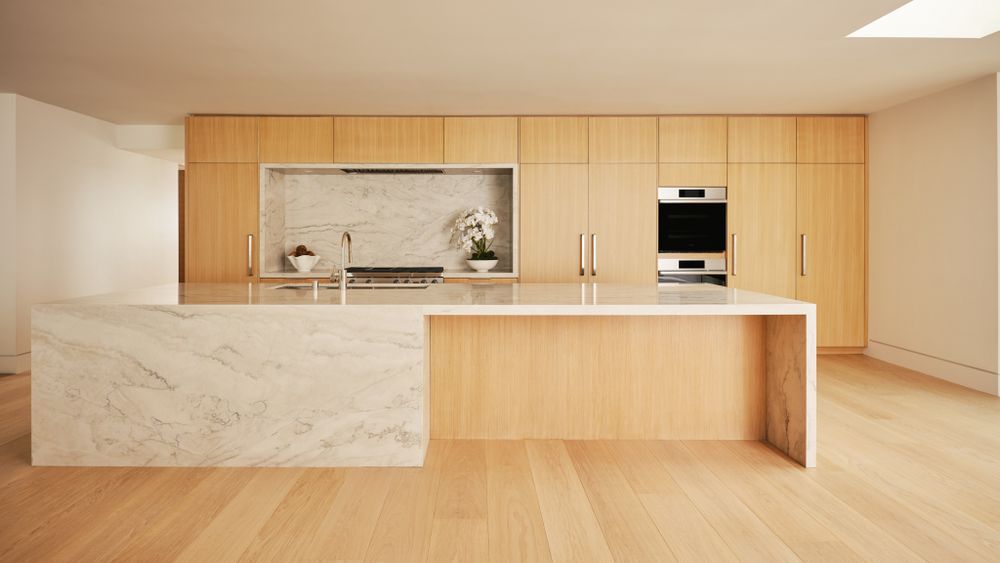 Minimalist kitchen with natural oak cabinetry, marble island, and clean lines — luxury design captured by Khoi Ly.
