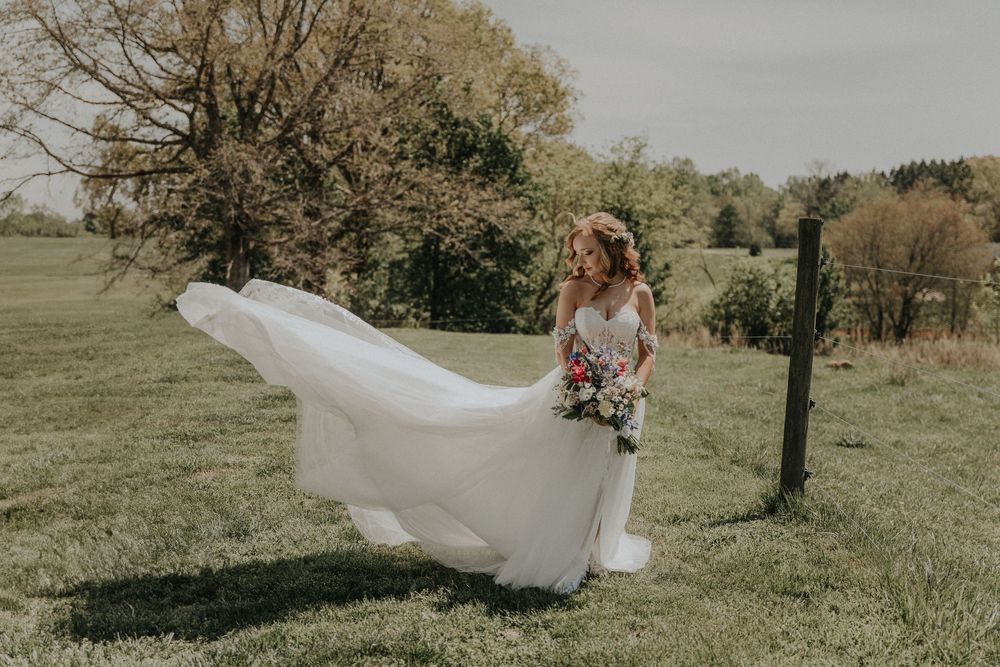 White wedding dress flowing dramatically in the wind across a sunny meadow landscape.