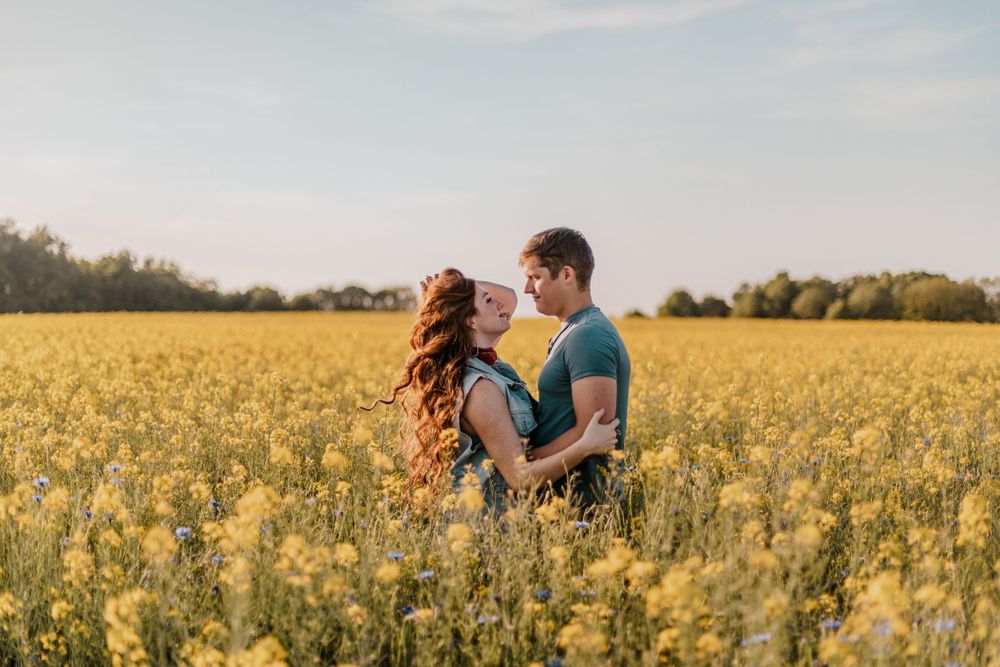Romantic couple embracing in a blooming yellow canola field at sunset.