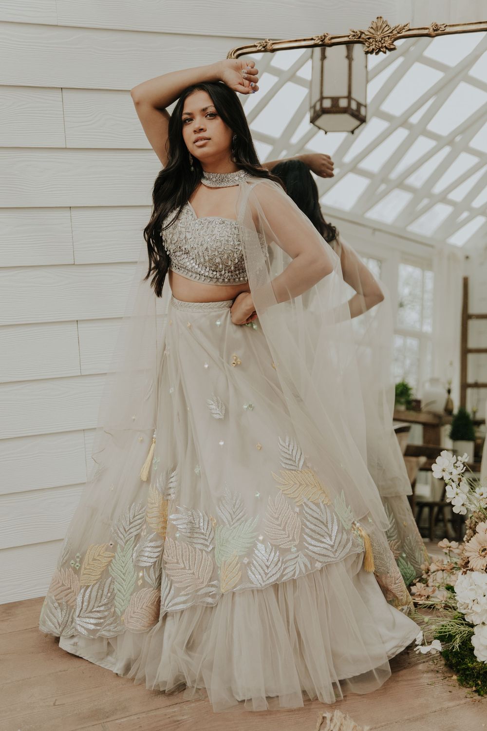 Elegant white lehenga with silver leaf embroidery twirls in a sunlit greenhouse setting.
