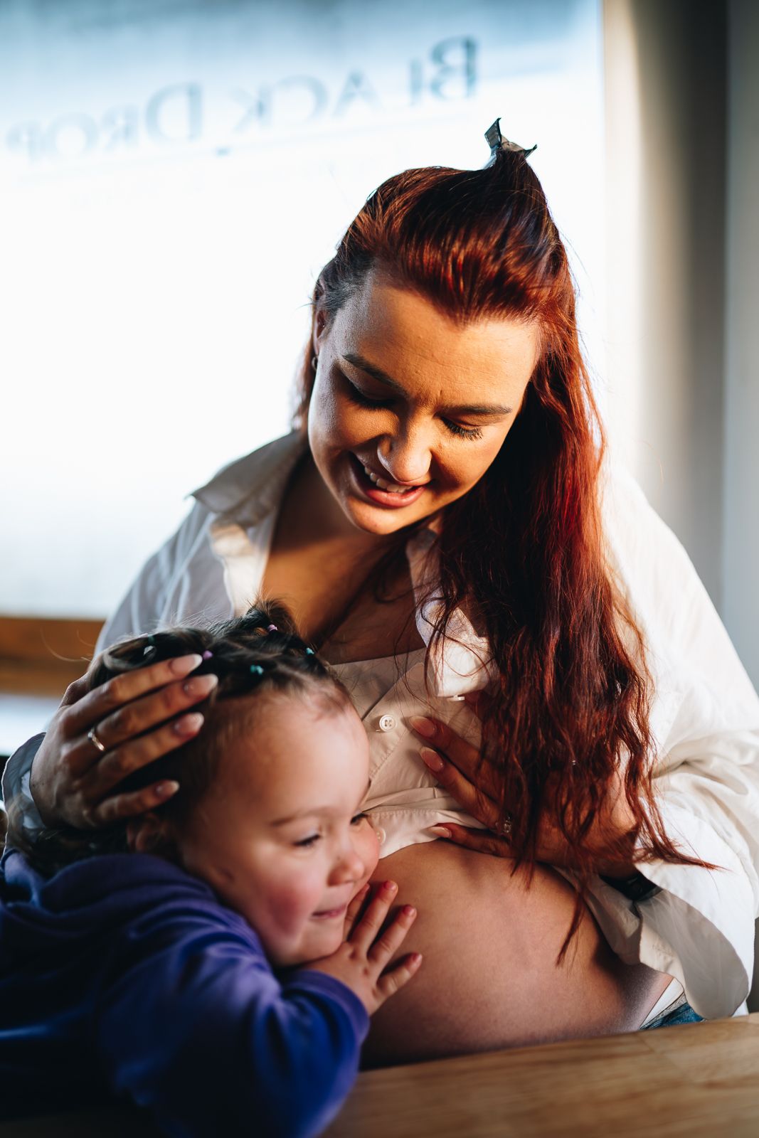 A tender moment between a pregnant woman and a small child listening to her belly in warm lighting taken by Melbourne maternity photographer