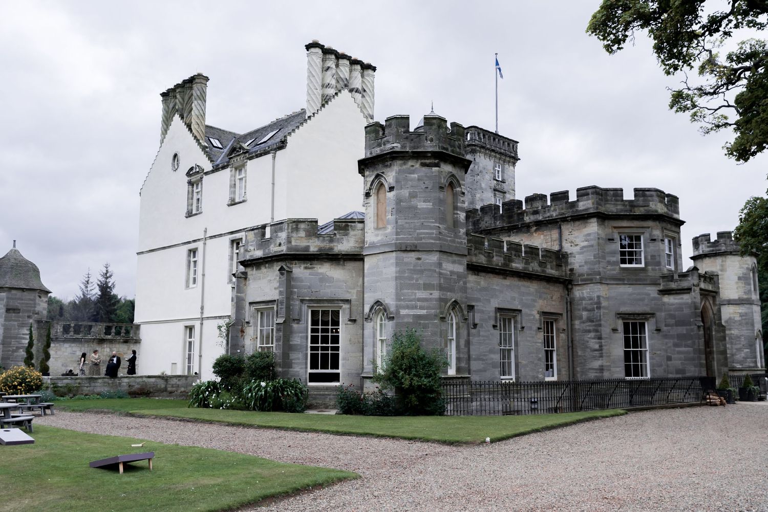 Historic Scottish baronial castle with white facade and grey stone turrets stands on manicured grounds under cloudy skies.