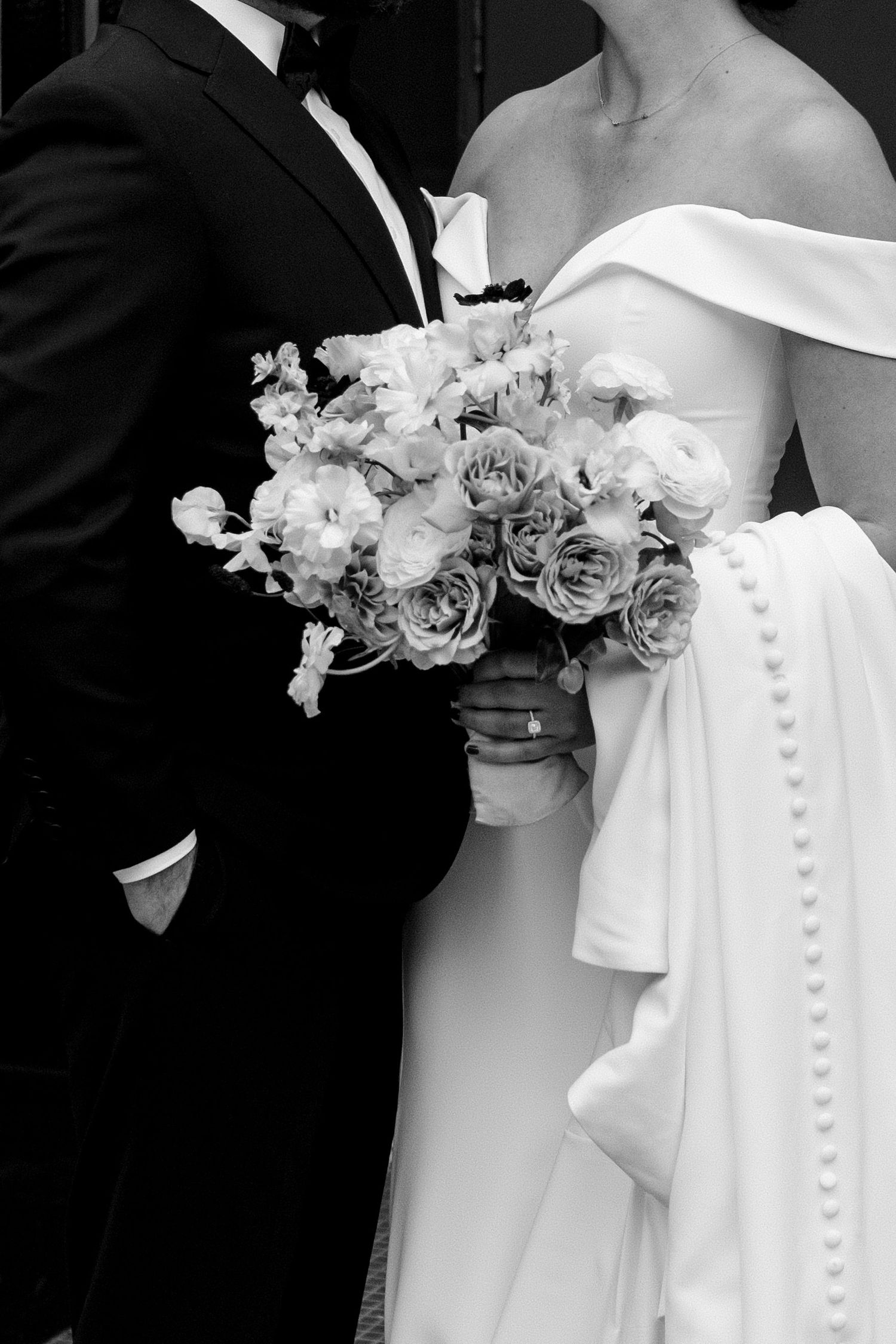 A black and white wedding photo showing a bouquet of roses held between the couple in formal attire.