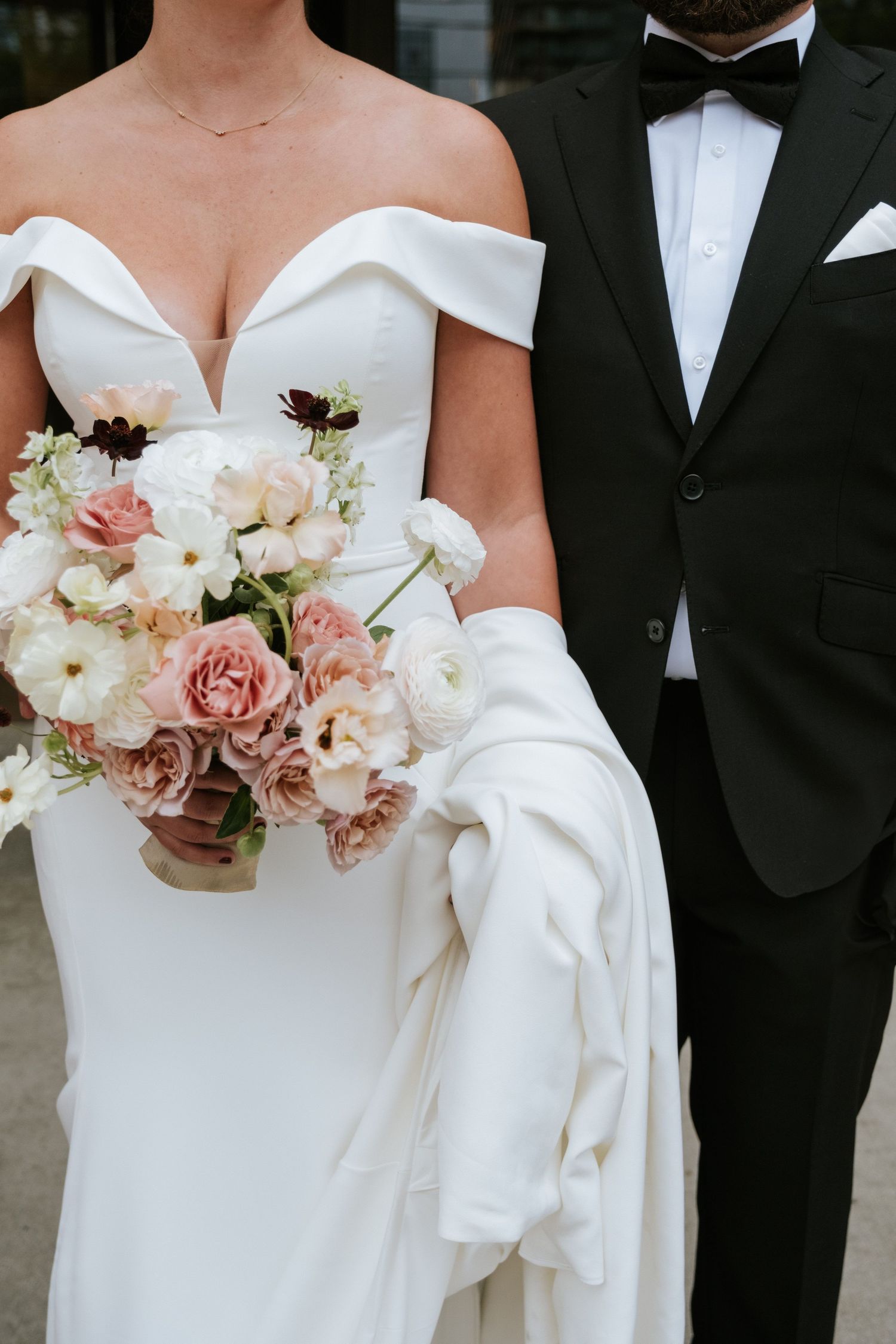 Close-up of bride's white dress and pink bouquet next to groom's classic tuxedo.