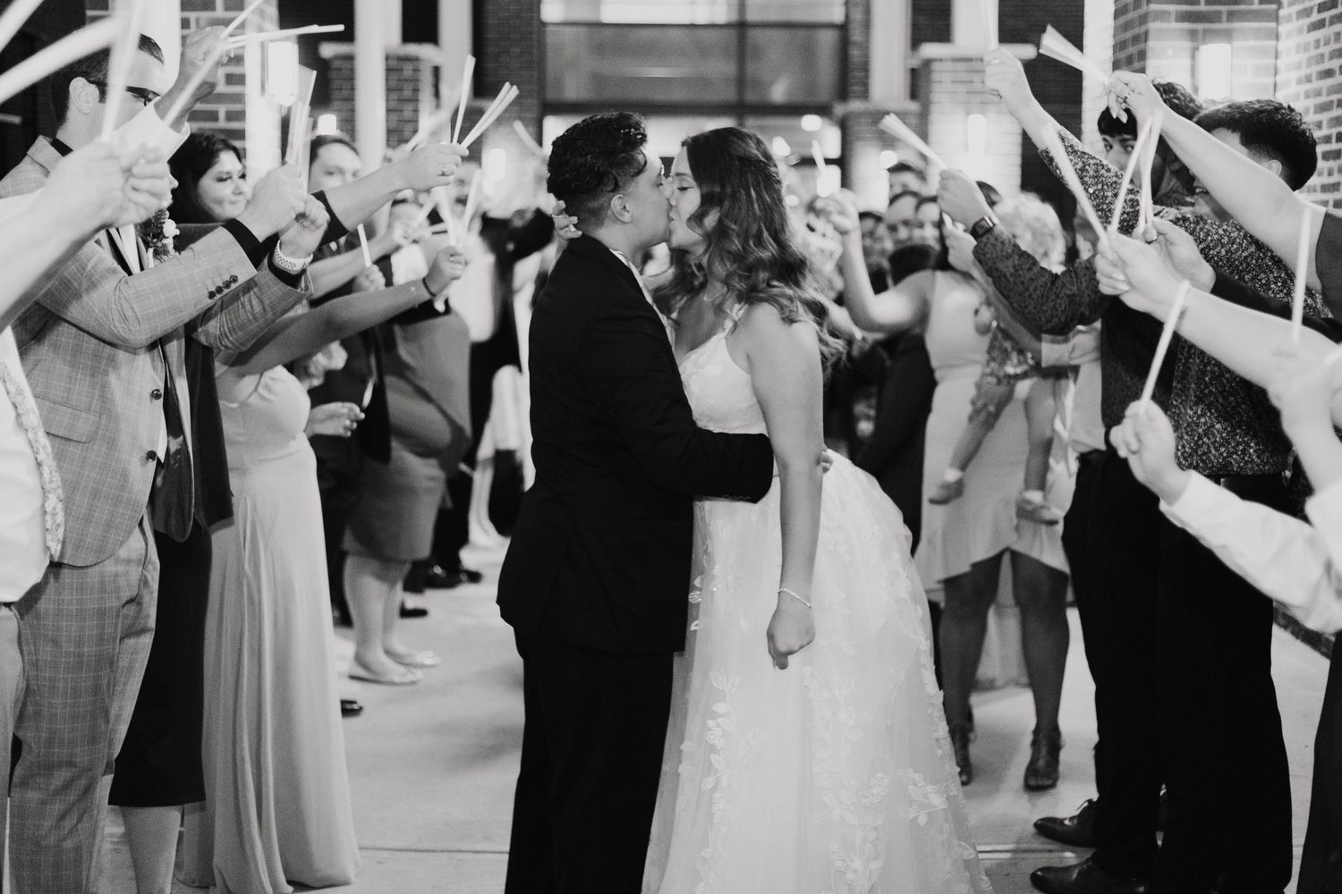 A bride and groom share an intimate moment at their wedding reception while guests wave sparklers in celebration.