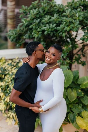 Intimate maternity moment captured between couple against garden backdrop.