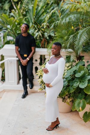 A maternity photoshoot featuring two people in contrasting black and white outfits amid tropical plants.