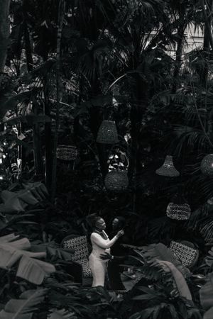 A black and white photo captures an expectant mother in a dreamy garden setting with hanging lanterns.