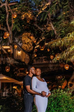 An intimate nighttime maternity portrait with warm lighting from overhead lanterns in trees.
