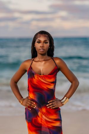 A beach portrait featuring someone in a flowing red and navy dress against the ocean at dusk.