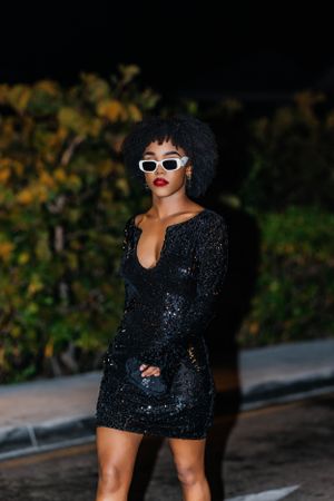 A fashion shot showcasing a sequined black dress and retro white sunglasses at night.