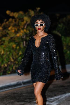 A stylish portrait in a glittering black dress with white sunglasses and natural hair.