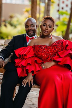 Glamorous couple in formal red dress and black suit pose outdoors.