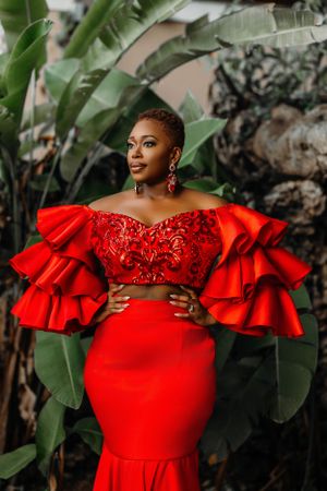 Elegant red two-piece gown with dramatic ruffled sleeves against a tropical garden backdrop.