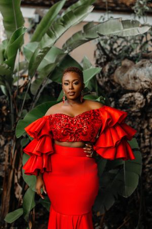 Stunning red formal dress with ruffled statement sleeves photographed in a lush tropical garden setting.