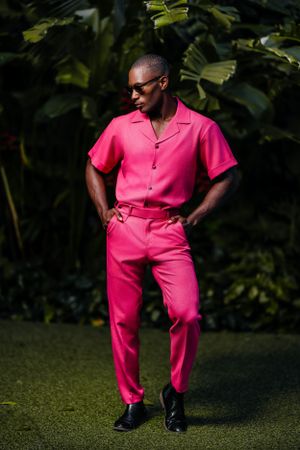 Model wearing elegant pink and white checkered suit with gloves poses in garden setting.