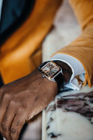 Close-up of silver square-faced watch on wrist with mustard sleeve and white cuff.
