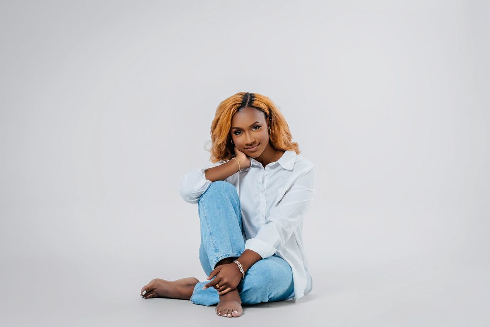 A playful portrait of someone in white shirt and blue jeans sitting cross-legged against white background.