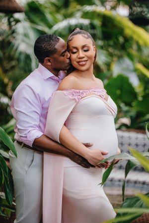 Romantic maternity photoshoot in a lush garden setting with pink off-shoulder dress.