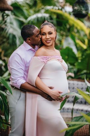 Tender maternity portrait in tropical garden with pink formal wear.