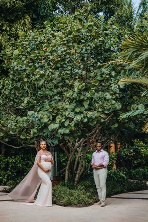 Elegant maternity photo with couple separated by tropical foliage.
