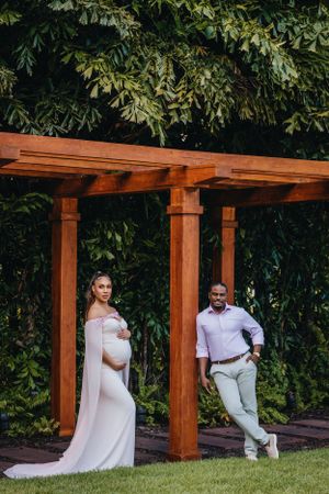 Maternity portrait under wooden pergola in garden setting.