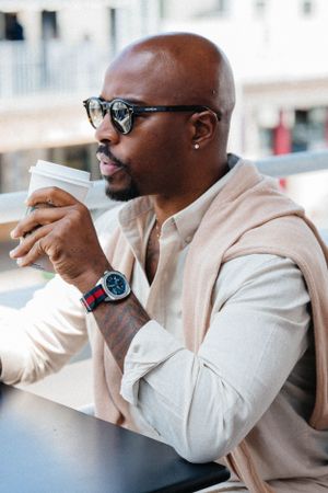 Professional enjoying coffee at outdoor cafe wearing beige outfit and smartwatch.
