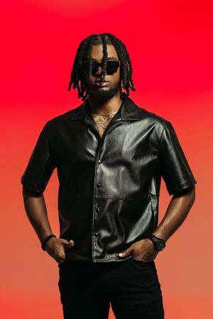 Stylish fashion portrait against vibrant red background featuring black leather shirt and sunglasses.