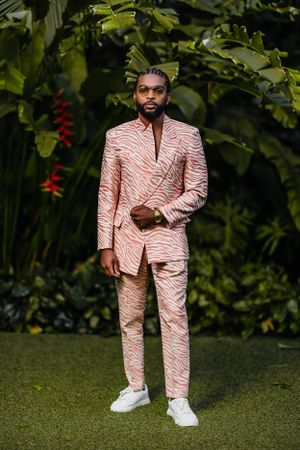 Model in pink zebra-print suit stands confidently against lush garden backdrop.