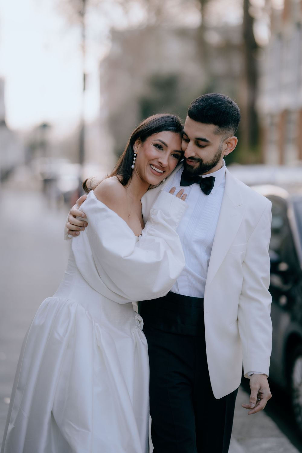 Newlyweds embrace lovingly outdoors, wearing classic white wedding attire.