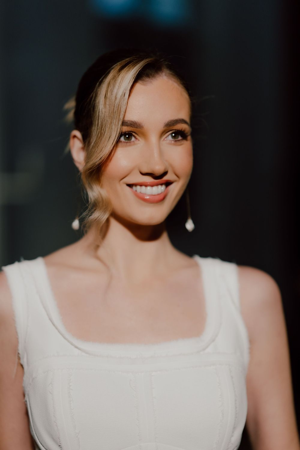 Portrait of person in white formal wear with pearl earrings and elegant updo.