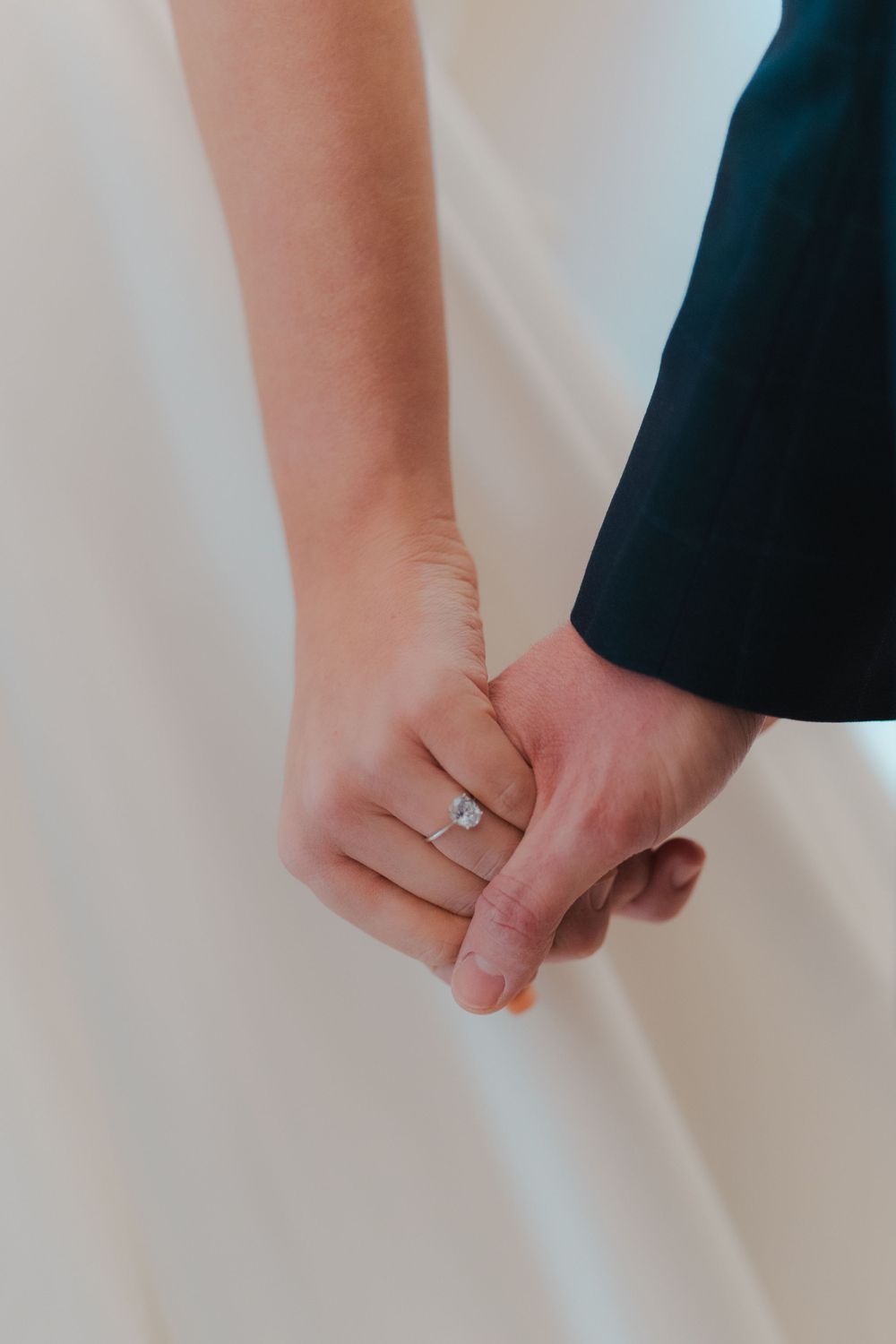 Close-up of couple holding hands showing wedding ring against white dress.