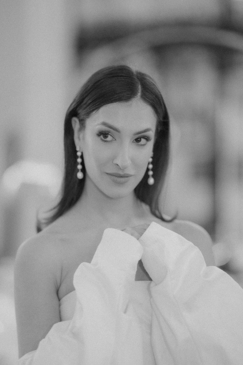Black and white portrait of person in strapless gown with dangling pearl earrings.
