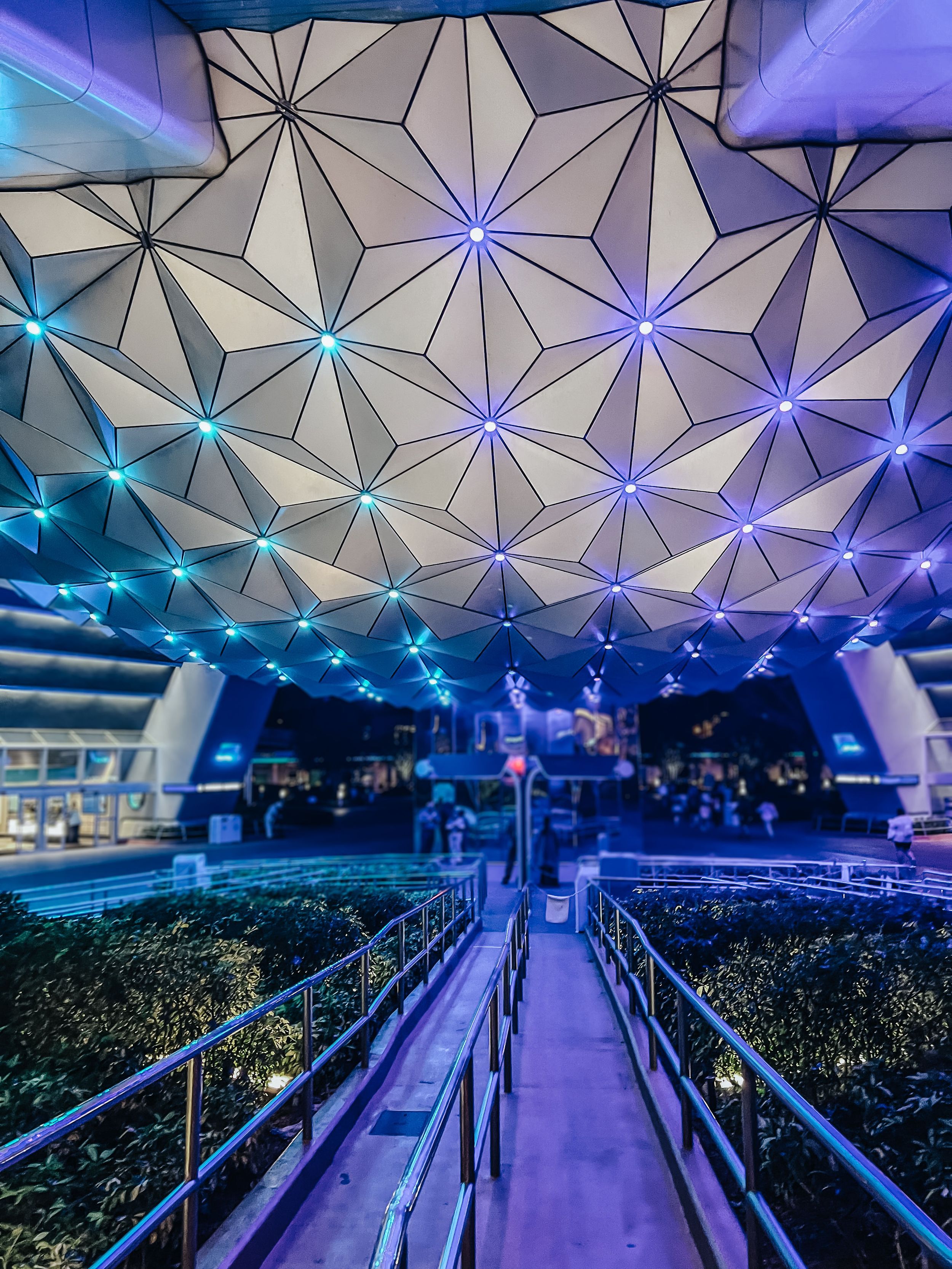 Futuristic space with geometric ceiling patterns illuminated by vibrant blue and purple lighting in an entertainment venue.