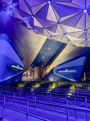Space Mountain attraction interior with modern geometric ceiling design illuminated in vibrant purple and blue lighting.