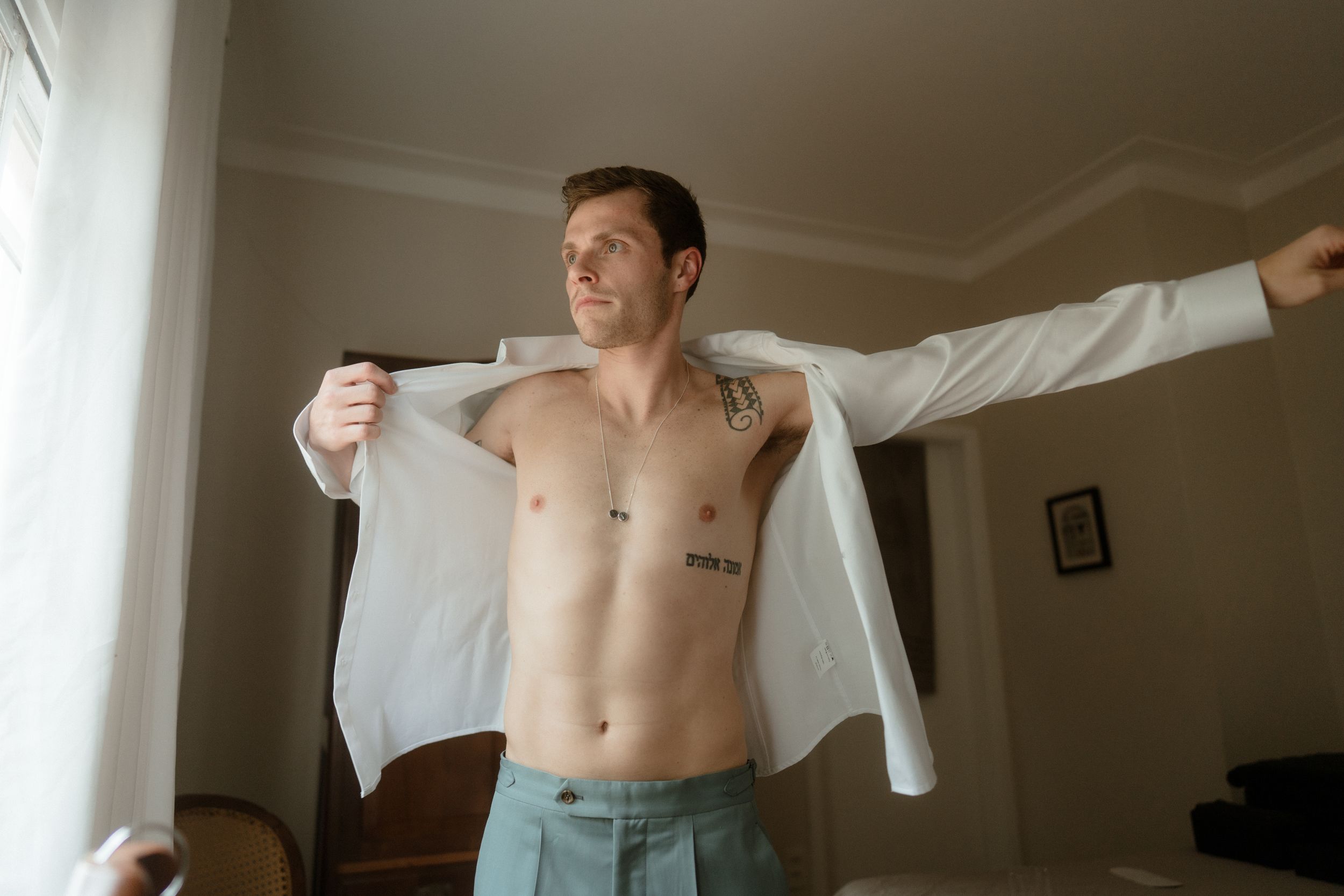 Preparing for formal event in bright bedroom with white dress shirt.