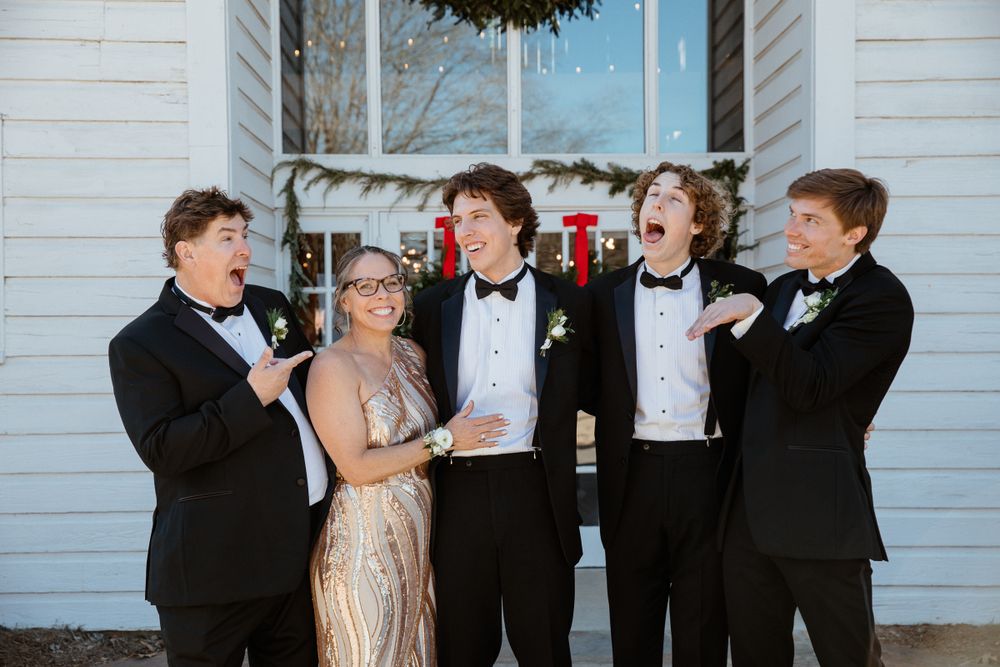 Wedding party members laughing and posing together outside a white building.