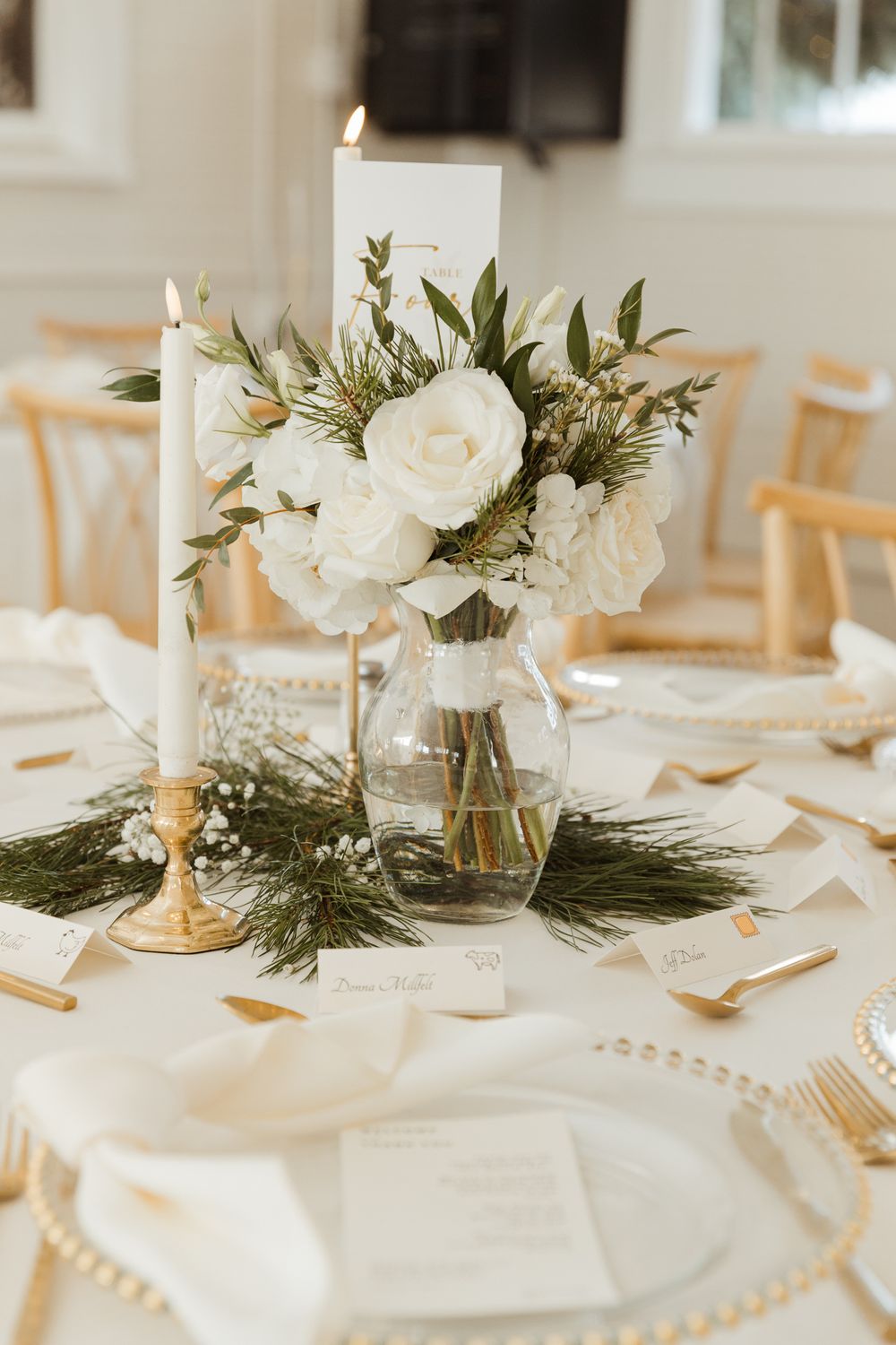 Elegant wedding table setting with white flowers, candles, and greenery centerpieces.