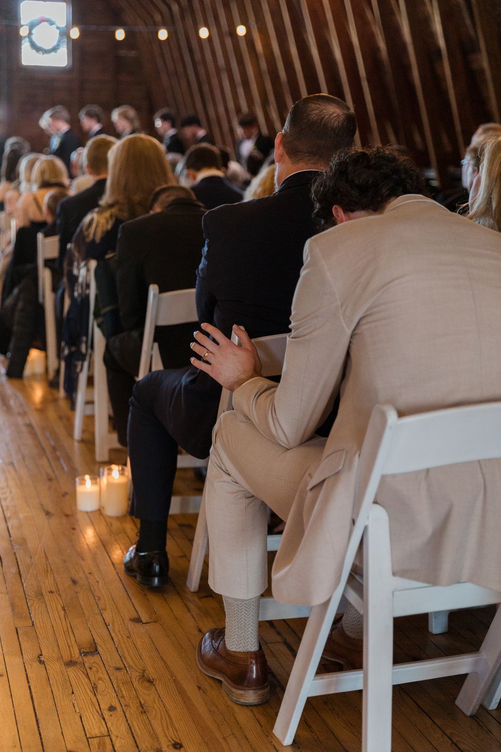 Wedding ceremony guests seated in white chairs inside a rustic wooden venue.